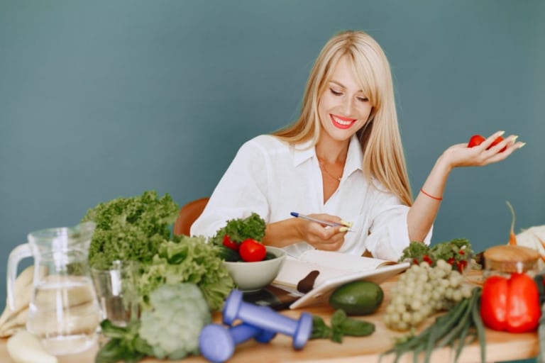 Woman sits in front of lots of green vegetables