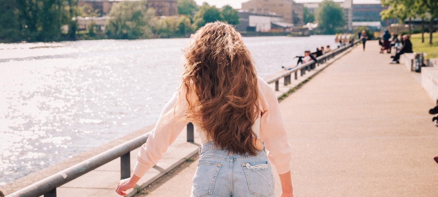 Frau mit Haarverlängerung #INSPOS mit braunen, langen Haaren geht neben einem Fluss